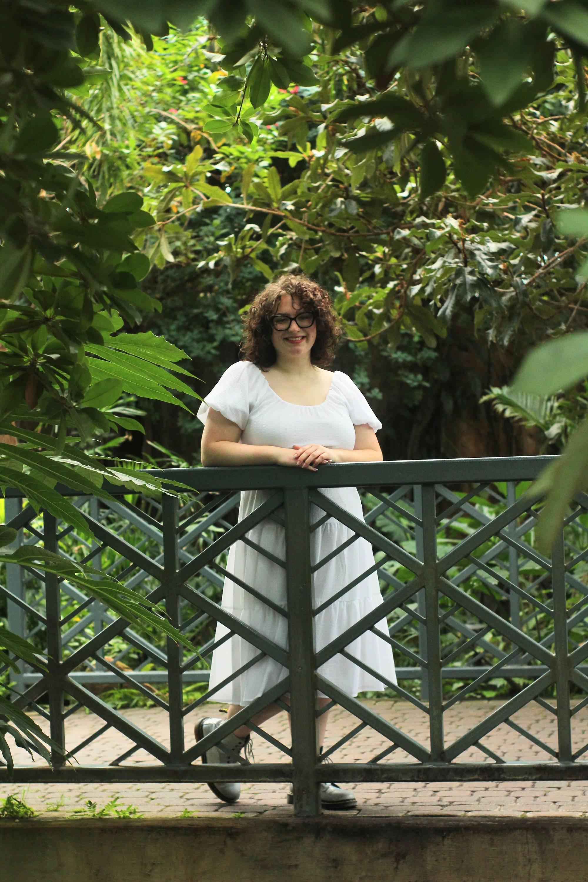 Woman with curly brown hair standing on a bridge surrounded by green foliage